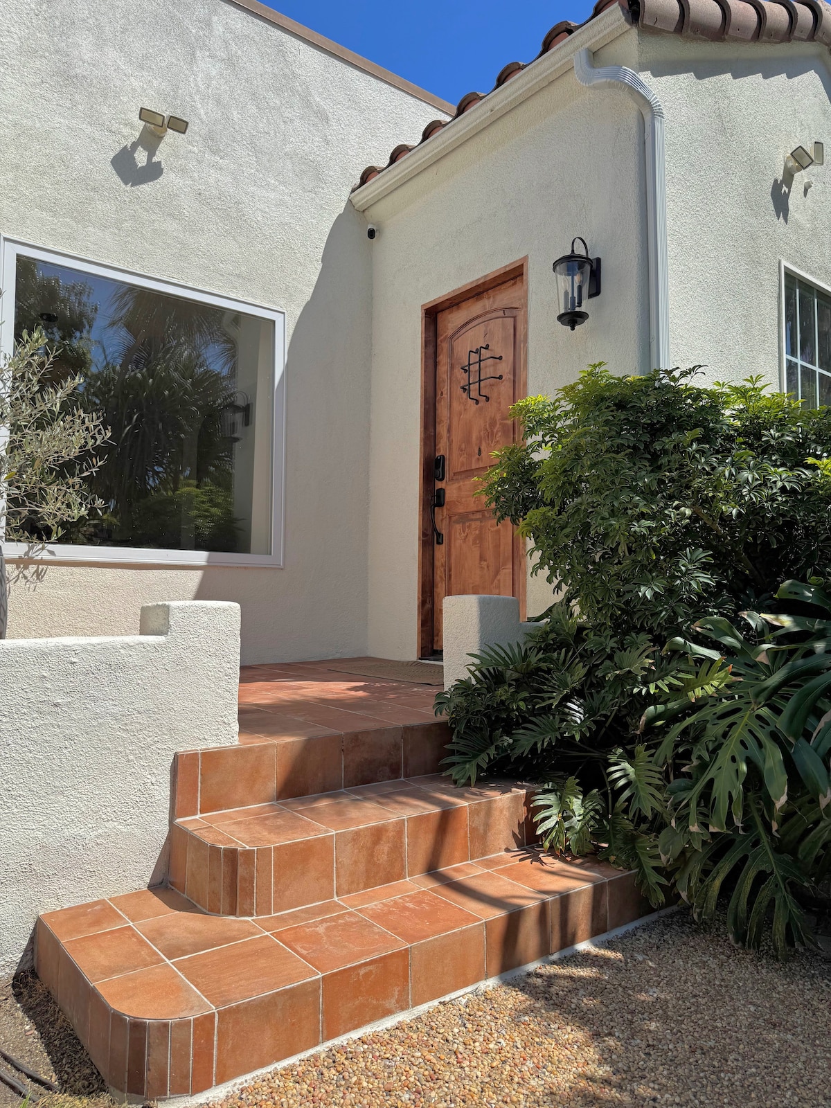 The front entry with terracotta tile steps, an arched wood door, and white stucco